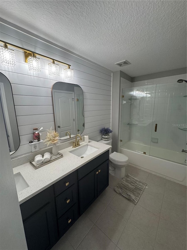 full bathroom featuring shower / bath combination with glass door, tile patterned flooring, vanity, a textured ceiling, and toilet