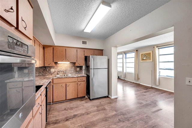 kitchen featuring appliances with stainless steel finishes, sink, decorative backsplash, a textured ceiling, and light hardwood / wood-style flooring