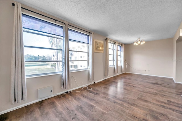 empty room featuring hardwood / wood-style floors, a textured ceiling, and an inviting chandelier