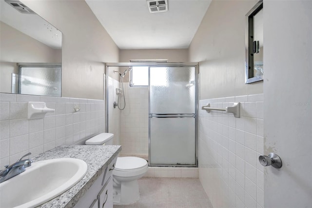 bathroom with tile walls, vanity, toilet, a shower with door, and tile patterned floors