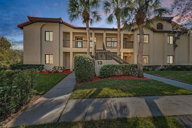 view of front of property featuring a tiled roof, a front yard, stairway, and stucco siding