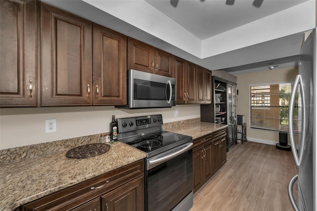 kitchen with dark brown cabinetry, light stone countertops, stainless steel appliances, and light hardwood / wood-style floors