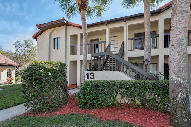 view of front facade featuring stairs, a tile roof, and stucco siding