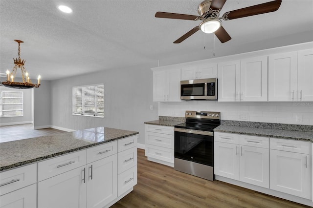 kitchen featuring appliances with stainless steel finishes, backsplash, dark hardwood / wood-style floors, white cabinets, and decorative light fixtures