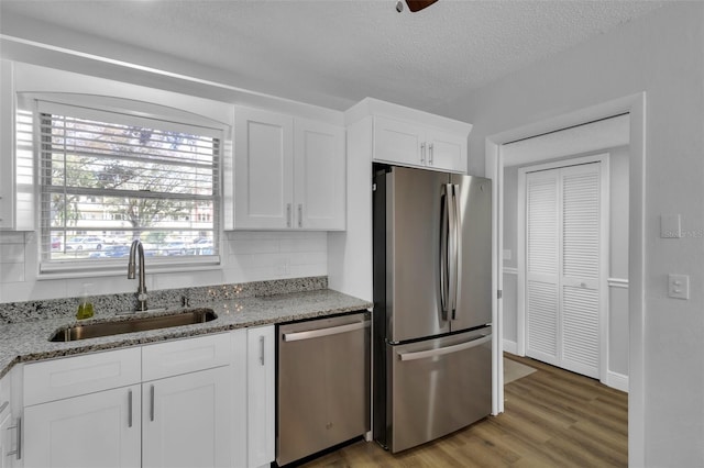 kitchen featuring sink, light stone counters, appliances with stainless steel finishes, light hardwood / wood-style floors, and white cabinets