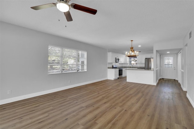 unfurnished living room with plenty of natural light, dark hardwood / wood-style flooring, ceiling fan with notable chandelier, and a textured ceiling