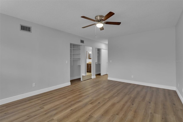 unfurnished bedroom featuring ceiling fan, two closets, light hardwood / wood-style flooring, and a textured ceiling