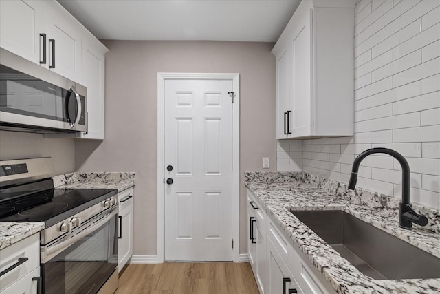 kitchen with sink, white cabinetry, light stone counters, light hardwood / wood-style flooring, and stainless steel appliances