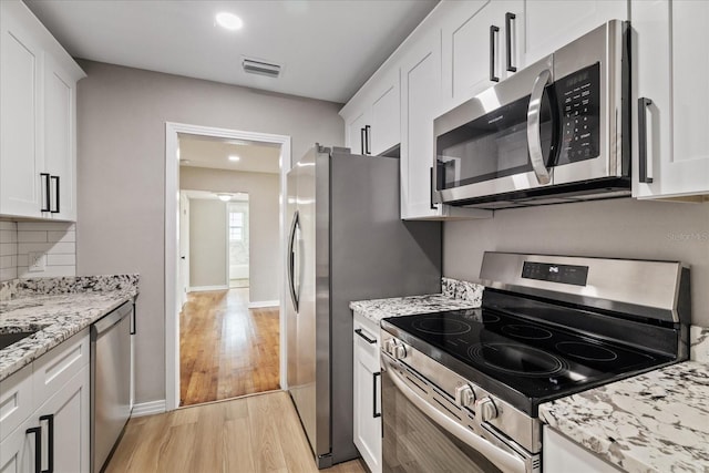 kitchen featuring appliances with stainless steel finishes, white cabinetry, backsplash, light stone counters, and light wood-type flooring