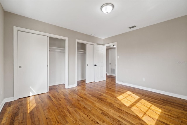 unfurnished bedroom featuring hardwood / wood-style flooring and multiple closets