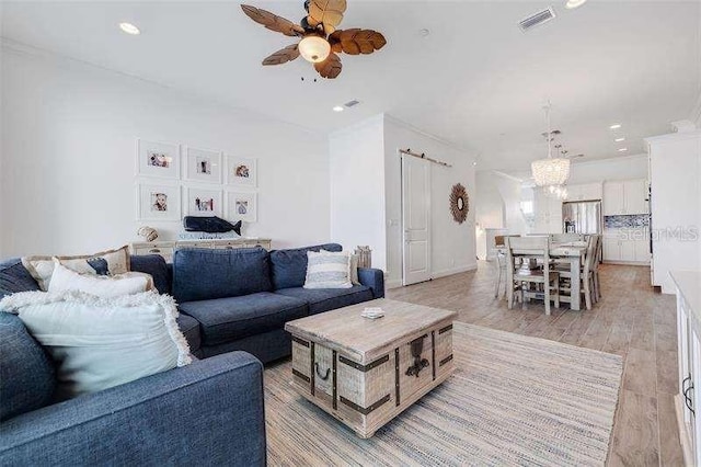 living room with ceiling fan with notable chandelier and light hardwood / wood-style floors