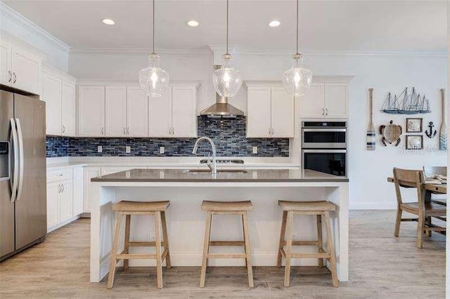 kitchen with white cabinets, appliances with stainless steel finishes, hanging light fixtures, and a center island with sink