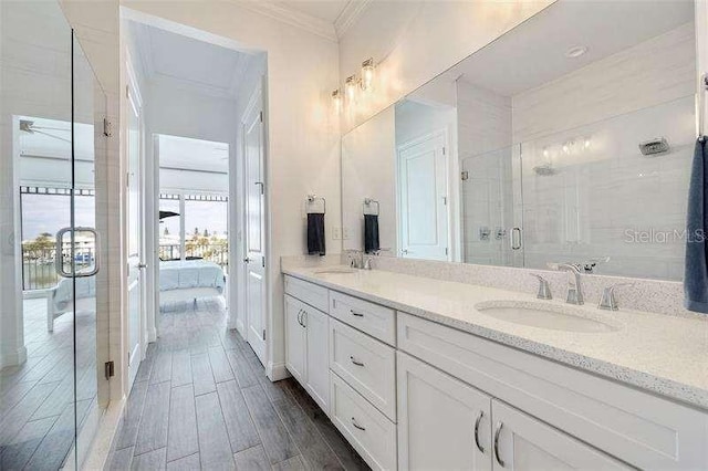 ensuite bathroom featuring crown molding, wood tiled floor, a shower stall, and a sink