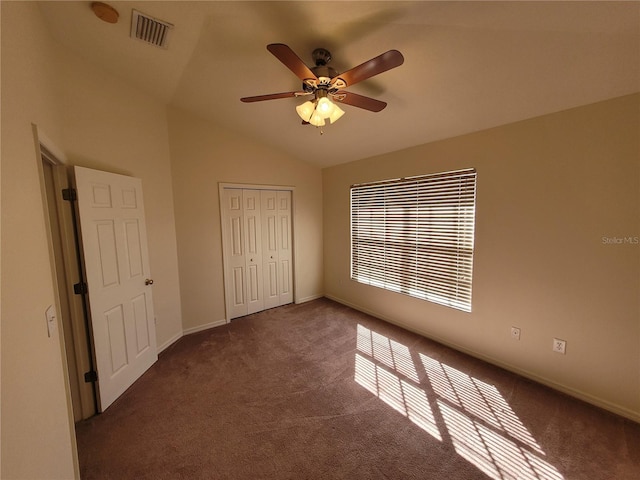 unfurnished bedroom featuring dark colored carpet, vaulted ceiling, ceiling fan, and a closet