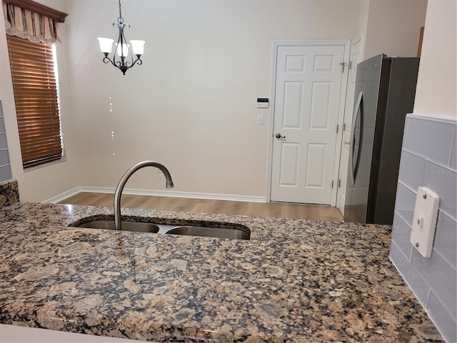 kitchen featuring hanging light fixtures, sink, stainless steel refrigerator, and light hardwood / wood-style flooring