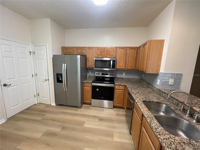 kitchen with dark stone countertops, sink, light hardwood / wood-style floors, and appliances with stainless steel finishes