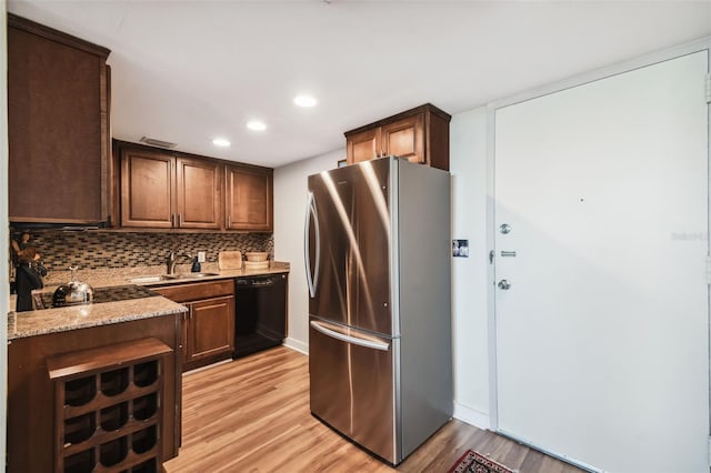 kitchen with sink, stainless steel fridge, black dishwasher, light stone countertops, and decorative backsplash