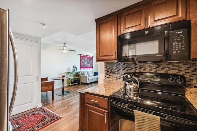 kitchen featuring light stone counters, backsplash, black appliances, and light hardwood / wood-style floors