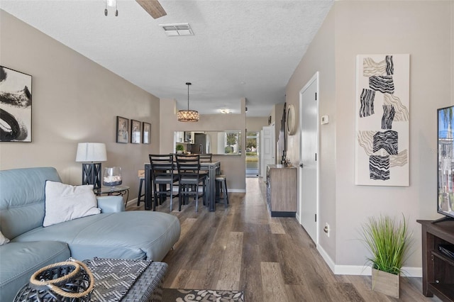 living room with dark hardwood / wood-style flooring, ceiling fan, and a textured ceiling