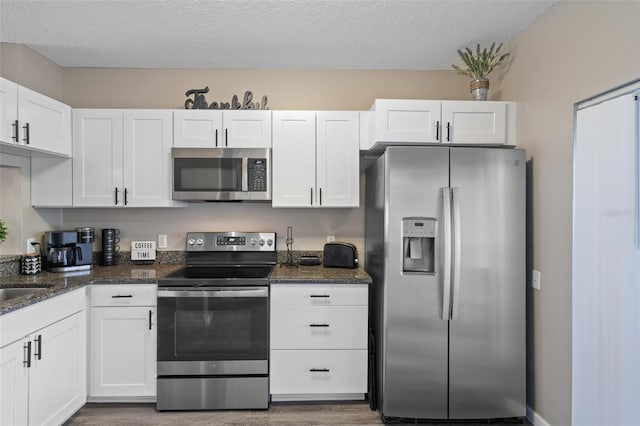 kitchen featuring white cabinetry, a textured ceiling, stainless steel appliances, and dark stone countertops