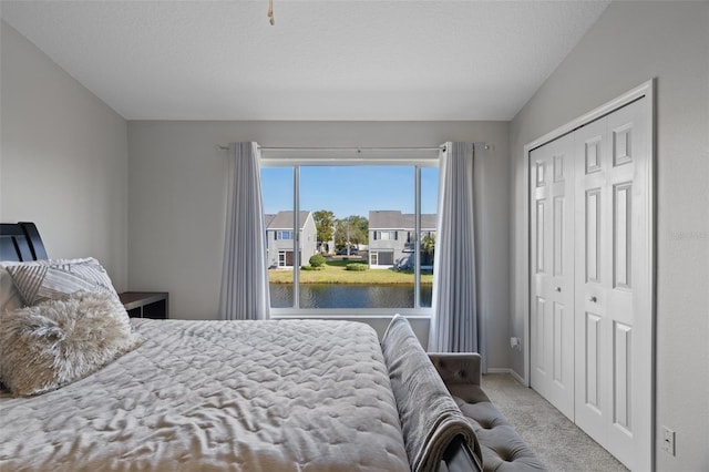 bedroom featuring a water view, light colored carpet, a closet, and a textured ceiling