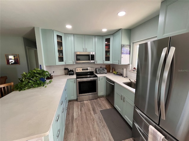 kitchen with appliances with stainless steel finishes, sink, decorative backsplash, and light wood-type flooring