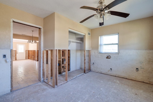 spare room with ceiling fan with notable chandelier and a textured ceiling