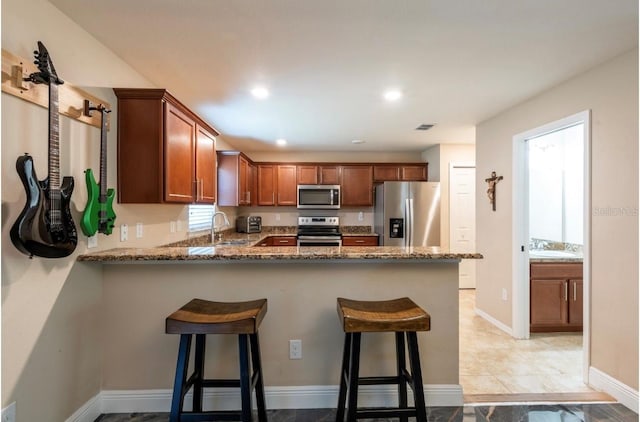 kitchen with sink, stainless steel appliances, a kitchen bar, kitchen peninsula, and dark stone counters