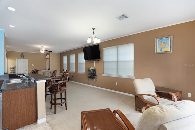 living area featuring light colored carpet, ceiling fan with notable chandelier, visible vents, baseboards, and ornamental molding