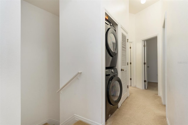 laundry room with stacked washer / drying machine, laundry area, light colored carpet, and baseboards