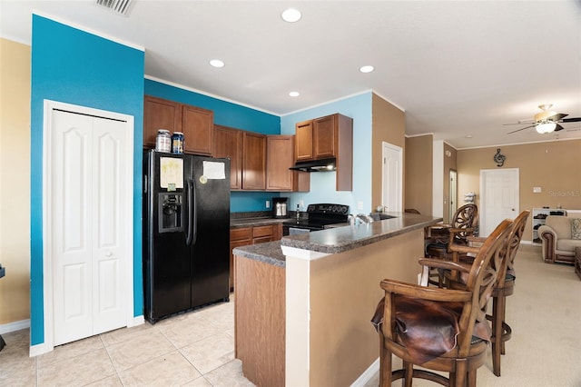 kitchen featuring a breakfast bar area, under cabinet range hood, a peninsula, black appliances, and dark countertops