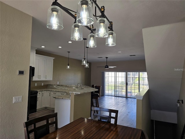 kitchen with wood-type flooring, a breakfast bar area, white cabinets, hanging light fixtures, and light stone counters