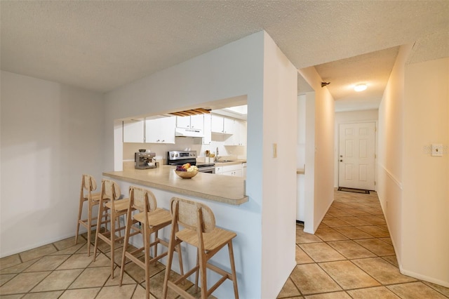 kitchen with stainless steel range with electric stovetop, a textured ceiling, light tile patterned floors, kitchen peninsula, and white cabinets