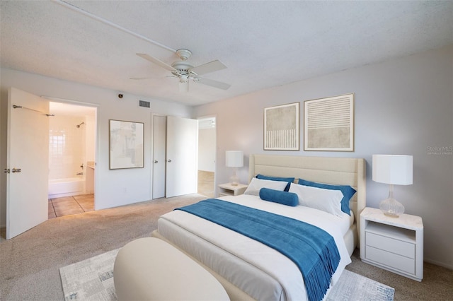 bedroom featuring connected bathroom, light colored carpet, a textured ceiling, and ceiling fan