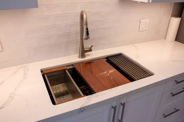 interior details with light stone counters, gray cabinets, sink, and backsplash