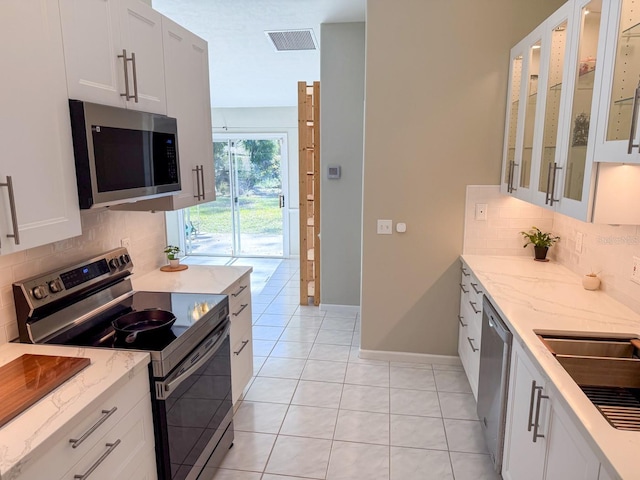 kitchen with appliances with stainless steel finishes, light tile patterned floors, white cabinets, and light stone counters