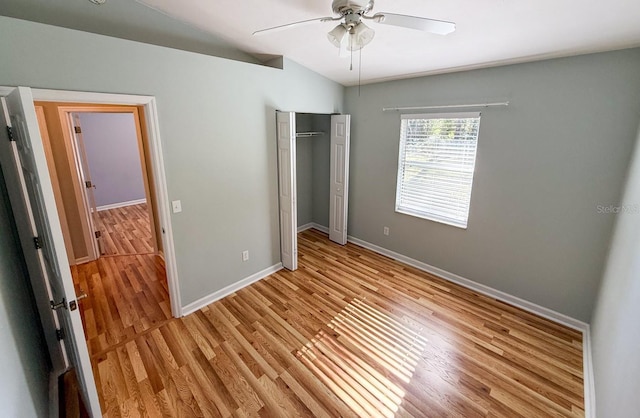 unfurnished bedroom featuring ceiling fan, lofted ceiling, a closet, and light wood-type flooring