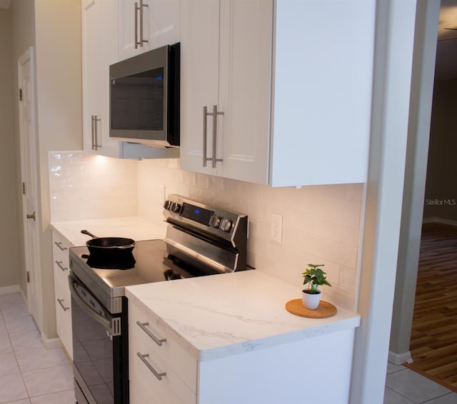5129 NW 30th Ln, Gainesville, FL 32606 - kitchen with stainless steel appliances, white cabinets, light tile patterned flooring, baseboards, and backsplash