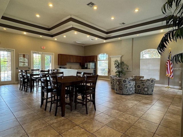 dining room with a raised ceiling, ornamental molding, a towering ceiling, and light tile patterned floors