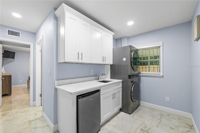 washroom featuring cabinets, stacked washing maching and dryer, and sink