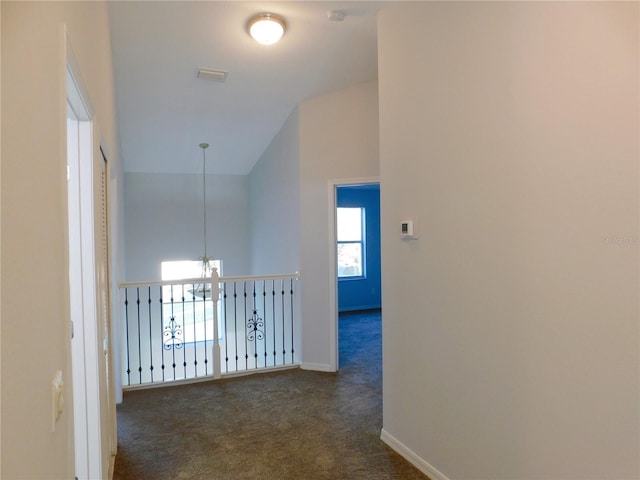 hall with lofted ceiling, a notable chandelier, and dark carpet