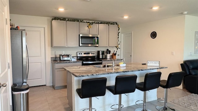 kitchen featuring light stone counters, stainless steel appliances, gray cabinets, and a center island with sink