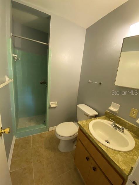 bathroom with vanity, a tile shower, tile patterned floors, and toilet