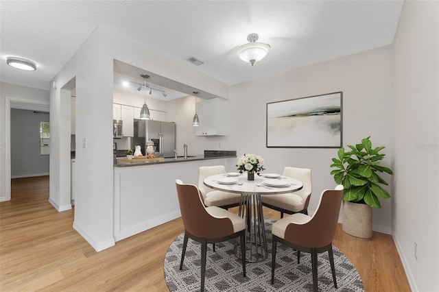 dining space with sink, light hardwood / wood-style flooring, and a textured ceiling