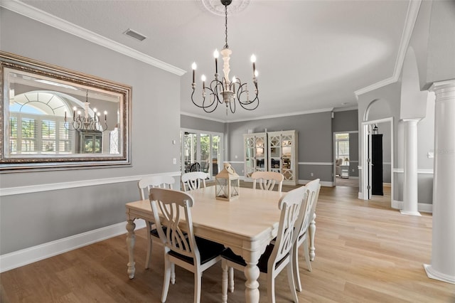 dining room featuring ornate columns, ornamental molding, a notable chandelier, and light hardwood / wood-style floors