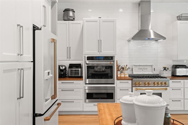 kitchen with wall chimney exhaust hood, white cabinetry, light hardwood / wood-style flooring, high quality appliances, and backsplash