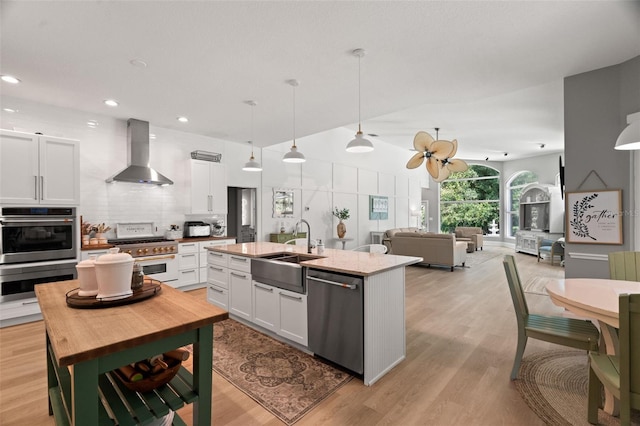 kitchen with wall chimney exhaust hood, sink, appliances with stainless steel finishes, pendant lighting, and white cabinets