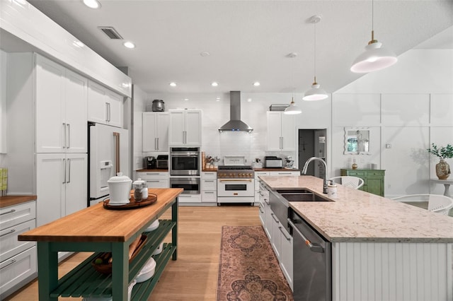 kitchen featuring white cabinetry, hanging light fixtures, high quality appliances, an island with sink, and wall chimney range hood