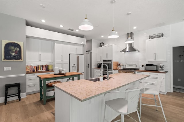 kitchen featuring decorative light fixtures, high end white refrigerator, sink, white cabinets, and light hardwood / wood-style floors