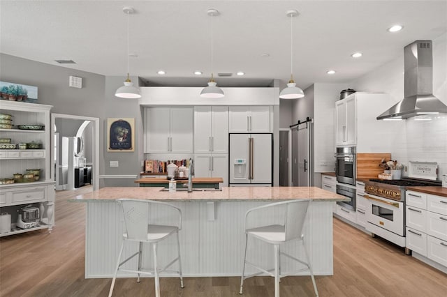 kitchen with high end appliances, island range hood, a barn door, and hanging light fixtures